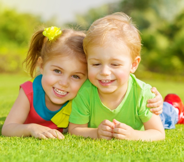 Image of two happy children having fun in the park, brother and sister lying down on green grass, best friends playing outdoors in spring, adorable little girl with cute boy enjoying springtime nature