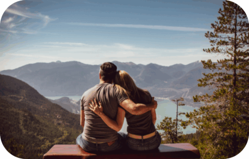 Para siedząca na ławce i obejmująca się podczas patrzenia na górski krajobraz