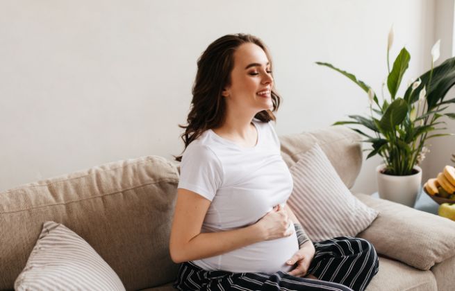 Jak wybrać najlepsze spośród badań NIPT, szczęśliwa kobieta w ciąży na kanapie